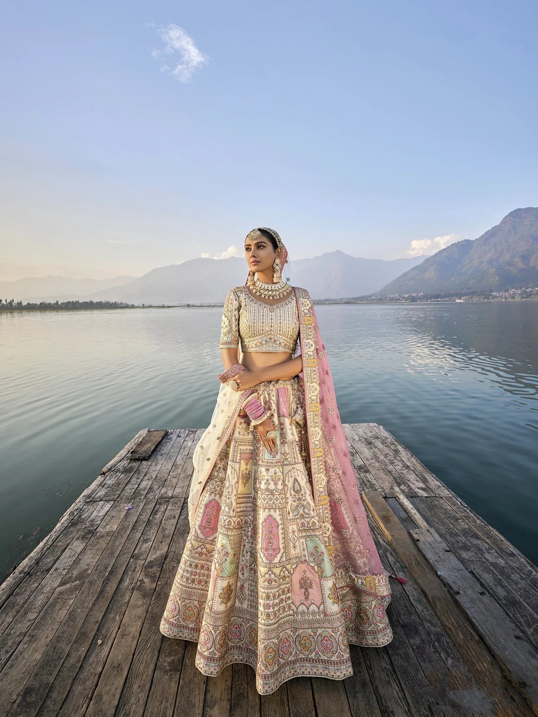 Woman in off-white silk lehenga with embroidered peach dupatta by a lake.