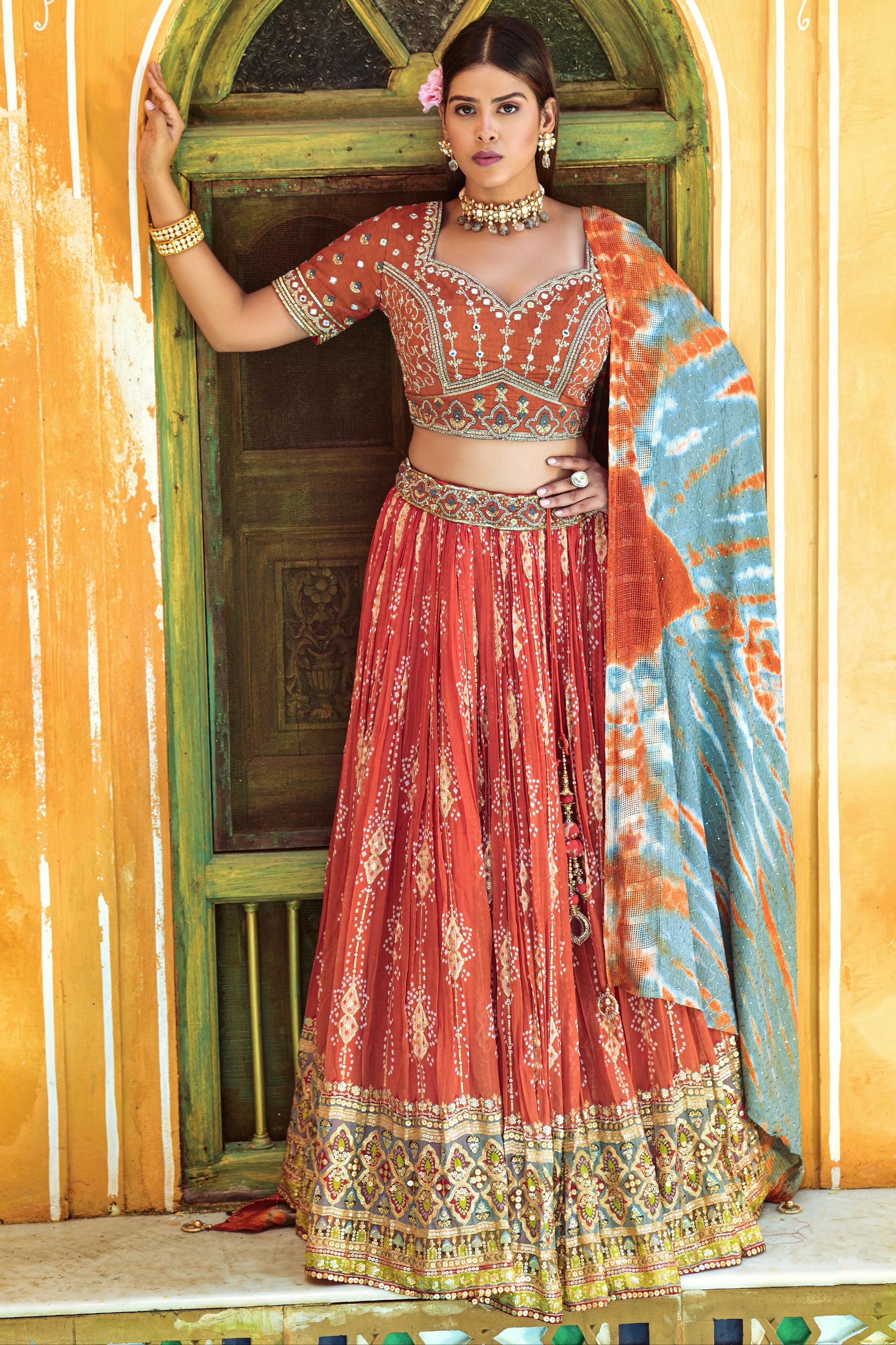 Woman wearing orange lehenga choli with digital print, mirror work, and sequence embellishments.