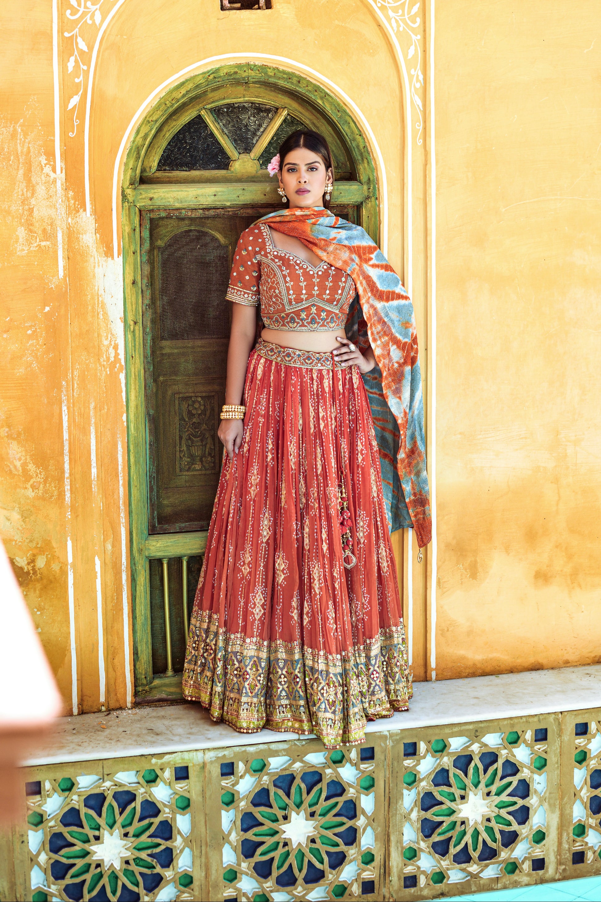 Woman wearing orange lehenga choli with digital print, mirror work, and sequence embellishments.