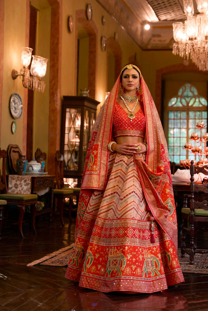 A woman wearing a traditional Indian wedding lehenga choli with mirror work, in a richly decorated room with elegant furnishings.