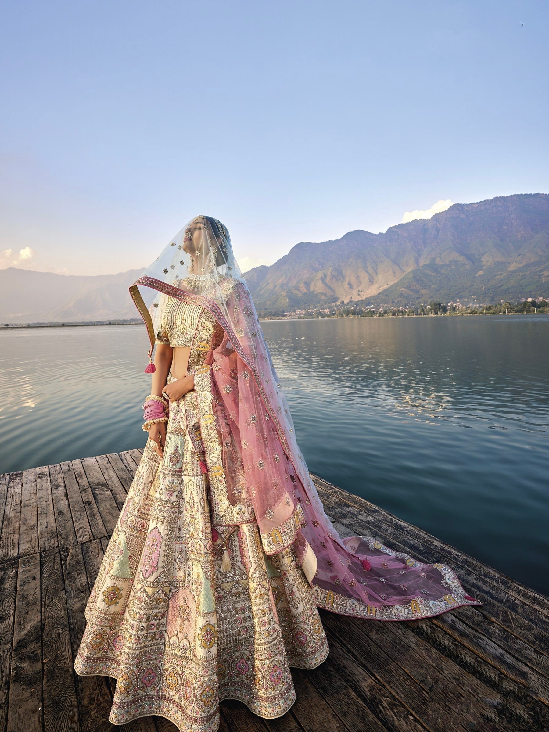 Woman in off-white silk lehenga with embroidered peach dupatta by a lake.