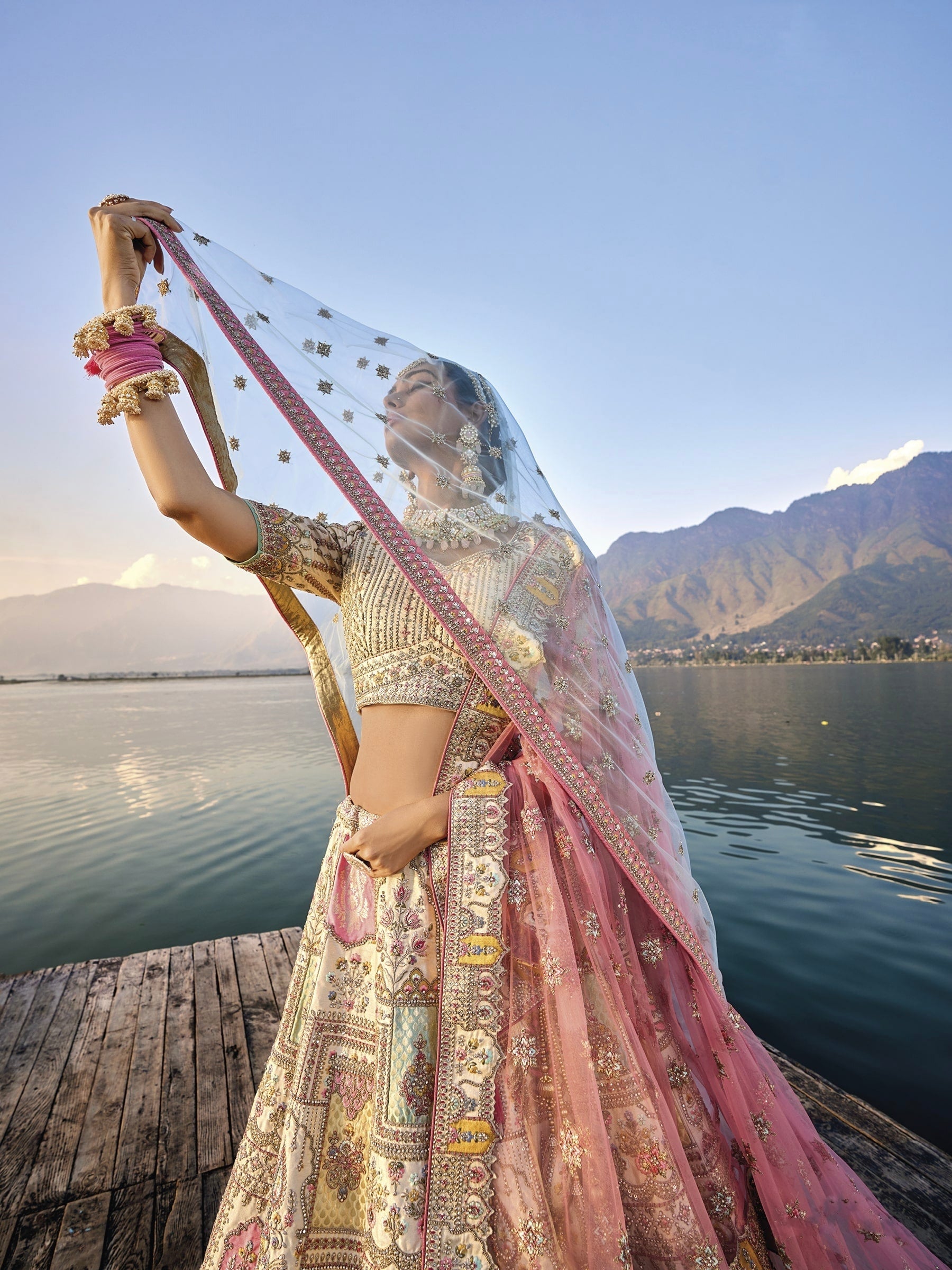 Woman in off-white silk lehenga with embroidered peach dupatta by a lake.