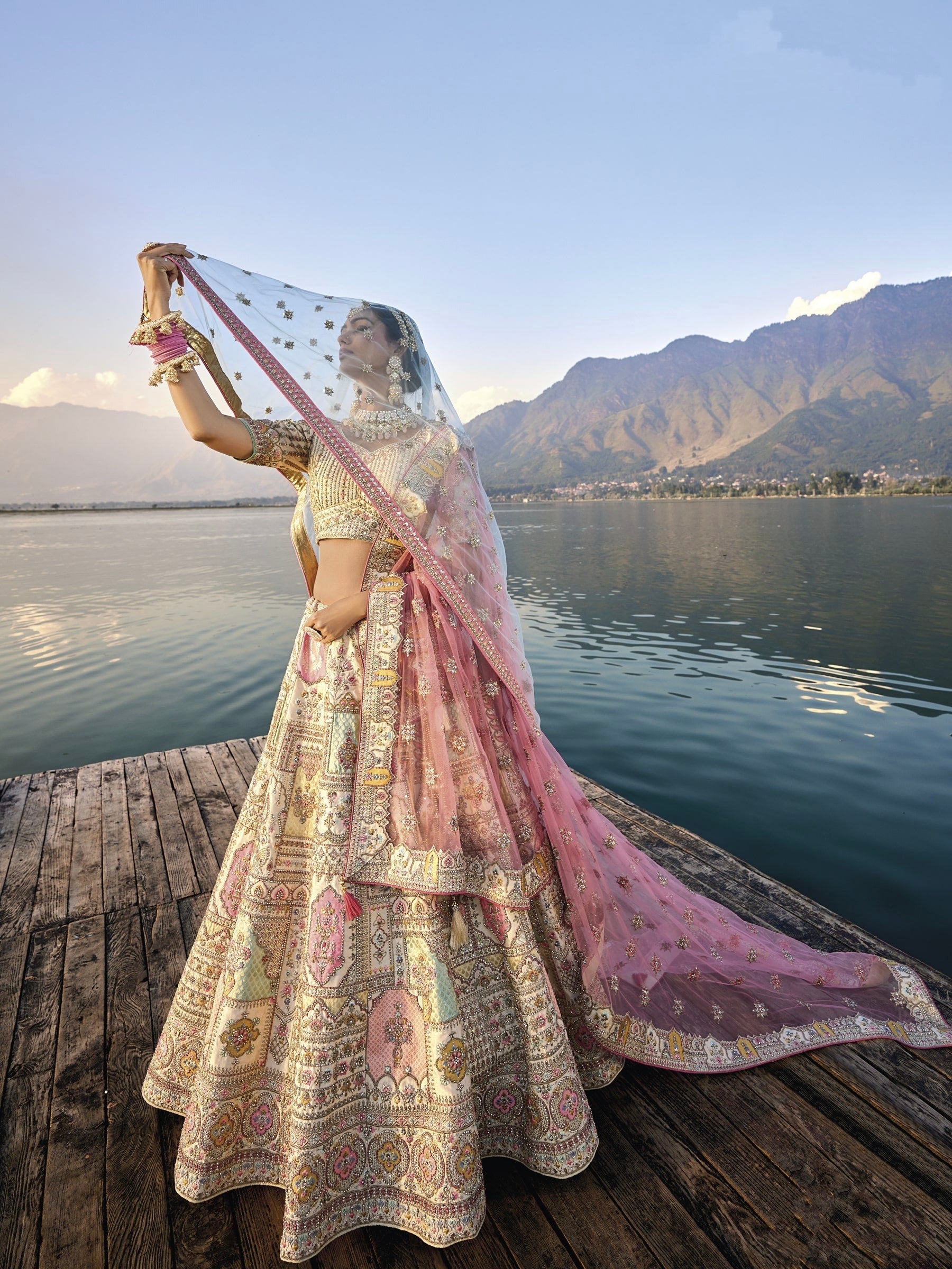 Woman in off-white silk lehenga with embroidered peach dupatta by a lake.