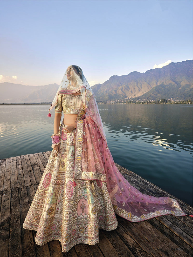 Woman in off-white silk lehenga with embroidered peach dupatta by a lake.