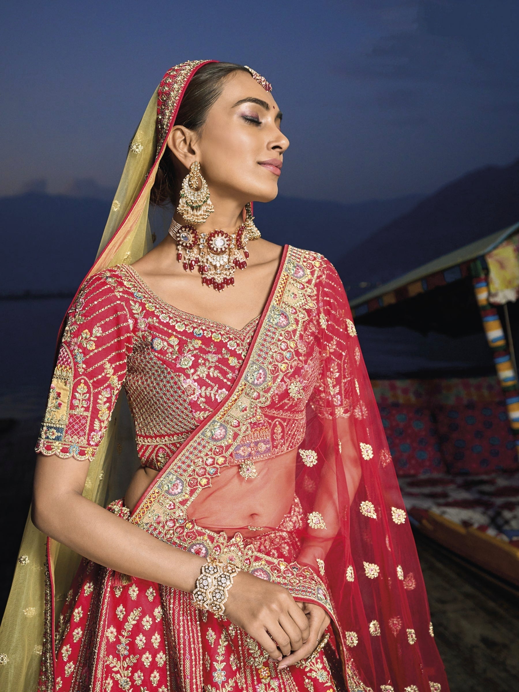 Woman in red silk lehenga with embroidered net dupatta by a lake.