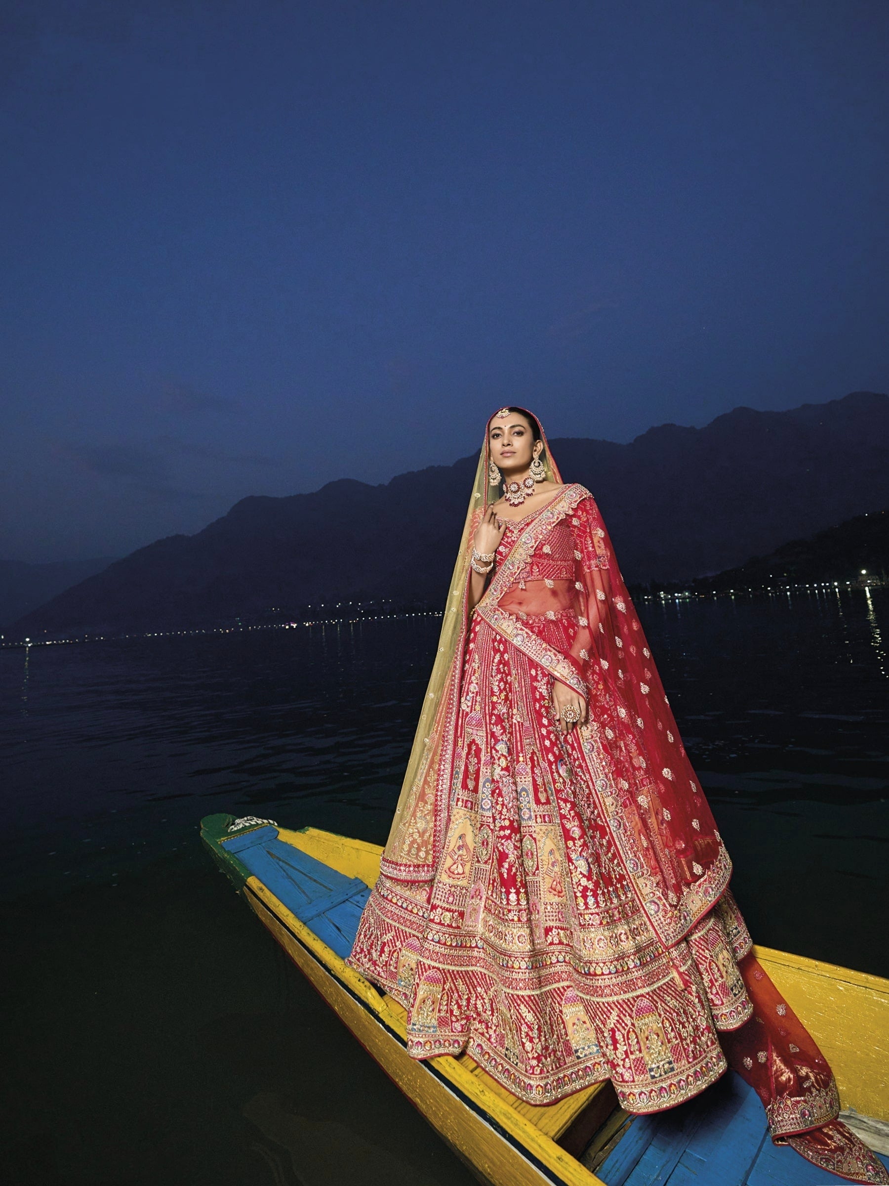 Woman in red silk lehenga with embroidered net dupatta by a lake.