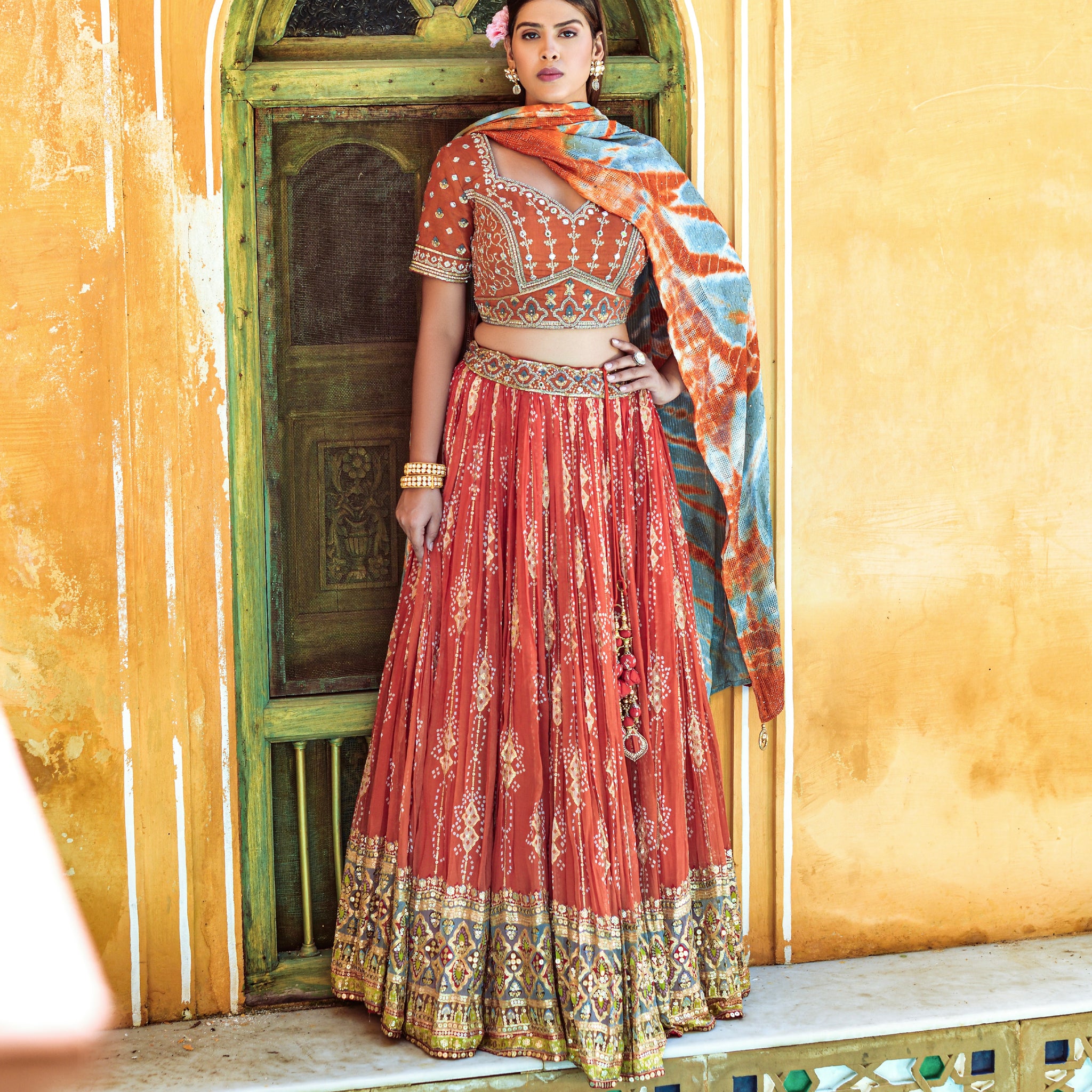 Woman wearing orange lehenga choli with digital print, mirror work, and sequence embellishments.